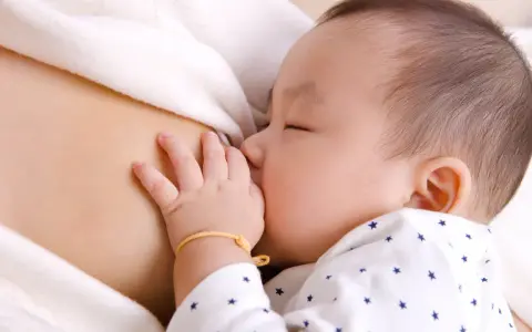 Bebé asiático durmiendo mientras se alimenta, mostrando el reflejo de succión. Su mano pequeña descansa sobre el pecho de su madre.