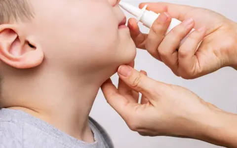 Una mano aplica spray nasal a un niño. La imagen ilustra cuántos lavados nasales se pueden hacer a un bebé para aliviar la congestión.
