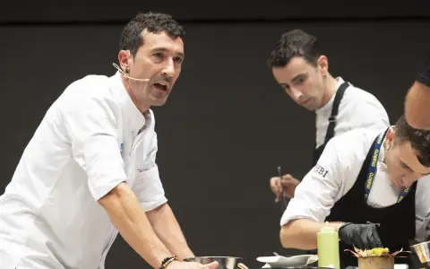 Eneko, chef con micrófono, dirige a su equipo en una demostración culinaria.