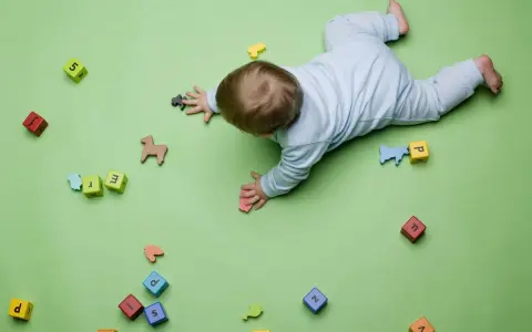 Bebé gateando entre bloques con letras y números, jugando con figuras de animales. Quizás buscando inspiración para nombres de niños originales.
