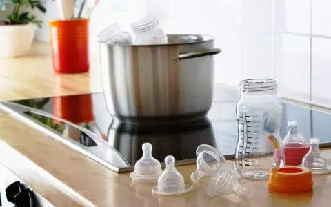 Preparación para desinfectar biberones con agua hirviendo. Tetinas y un biberón medidor listos en la encimera.