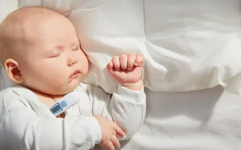 Bebé de 1 mes durmiendo con termómetro que marca 38.2°C, indicando un posible resfriado.
