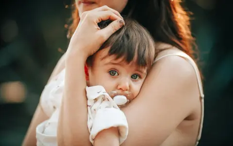 Bebé con chupete, acurrucado en brazos de su madre. Un momento tierno que nos hace pensar en cuando se inventó el chupete.