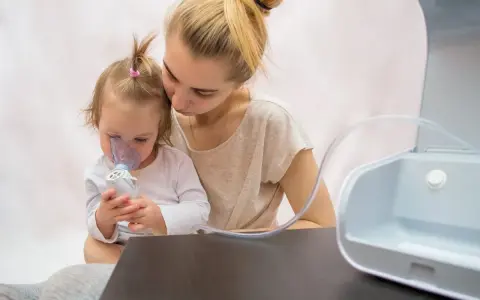 Madre consuela a su hija con bronquitis espástica mientras usa un nebulizador.