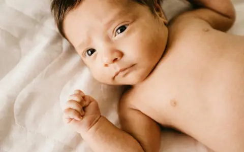 Bebé con mirada intensa, su puño cerrado y piel suave. Podría ser un signo de hipertonía en bebés, pero su expresión es serena.