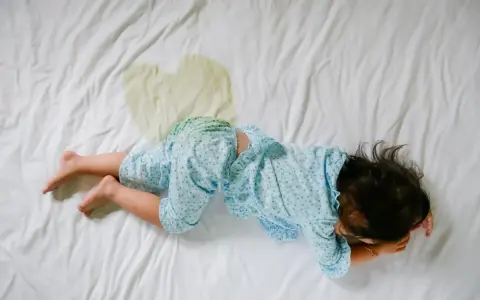 Niño en cama con mancha de orina. Buscando enuresis nocturna infantil remedios naturales para ayudarle.