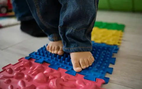 Pies descalzos de un niño sobre un tapete de rompecabezas texturizado, parte de juegos de coordinación para el desarrollo.