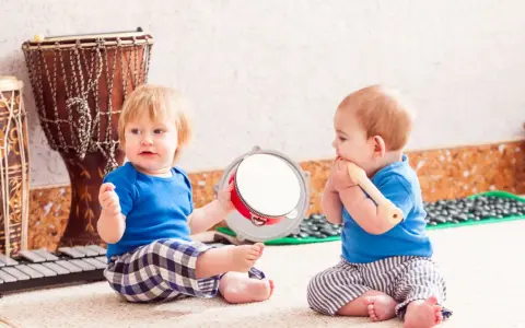 Dos bebés disfrutan de la estimulación musical temprana, uno con un tambor y otro con una flauta, rodeados de instrumentos.