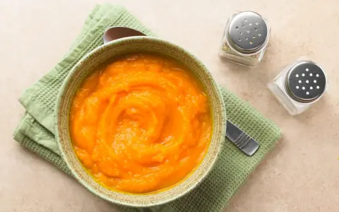 Puré de calabaza y patata para bebé, listo para congelar. Servido en un cuenco con una cuchara y saleros al lado.
