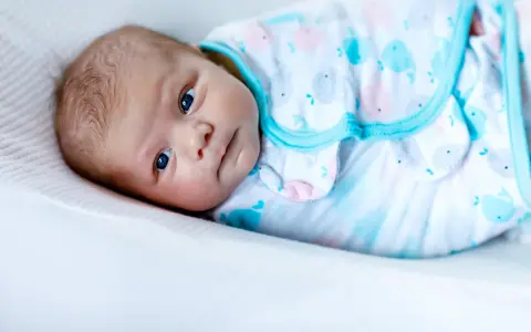 Un tierno bebé con ojos azules, envuelto en una mantita con ballenas, listo para arrullar.