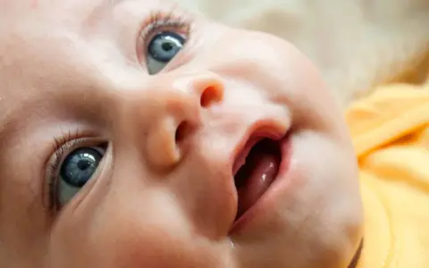 Bebé con ojos azules y boca abierta, mostrando las encías y los primeros dientes saliendo.
