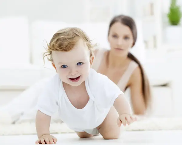 Bebé sonriente gateando, con su madre observando. Una escena tierna para estimular el gateo.