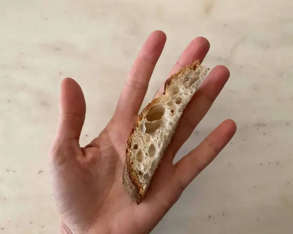 Una mano sostiene una rebanada de pan artesanal, perfecta para el primer pan para bebés.