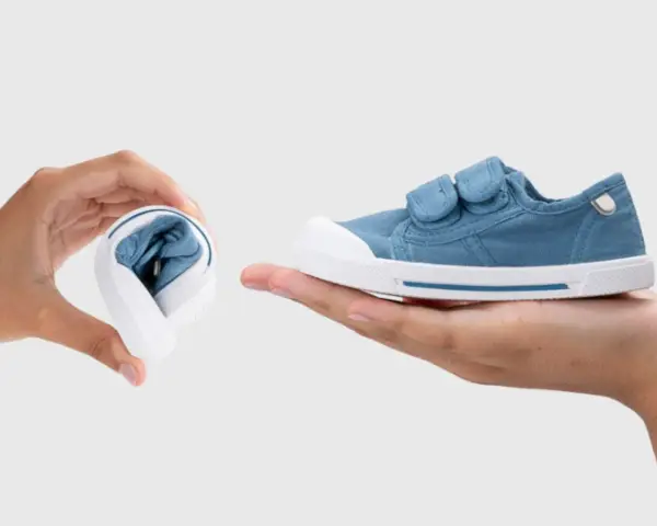 Manos muestran que son los escarpines: uno doblado y otro desplegado, de tela azul con velcro.