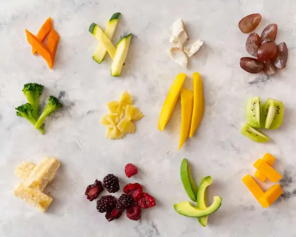 Variedad de alimentos para blw bebé 6 meses: zanahoria, calabacín, brócoli, pasta, mango, kiwi, aguacate, bayas, plátano y queso.