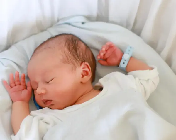Bebé recién nacido duerme plácidamente en su cuna. Su pulsera de identificación, con el **lua nombre**, indica que está seguro y cuidado.