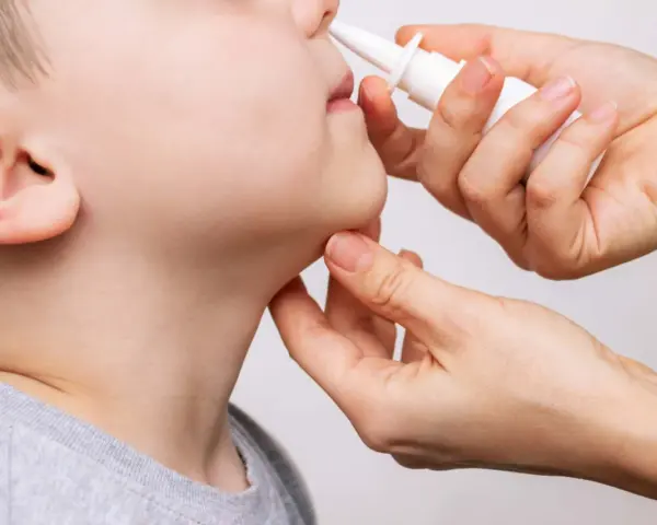 Una mano aplica spray nasal a un niño. La imagen ilustra cuántos lavados nasales se pueden hacer a un bebé para aliviar la congestión.