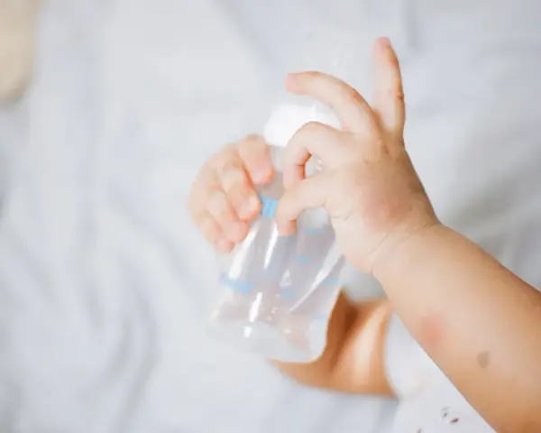 Manitas de bebé sujetando un biberón. Se aprecian rojeces en su piel, quizás por dermatitis o por el calor del sudor.