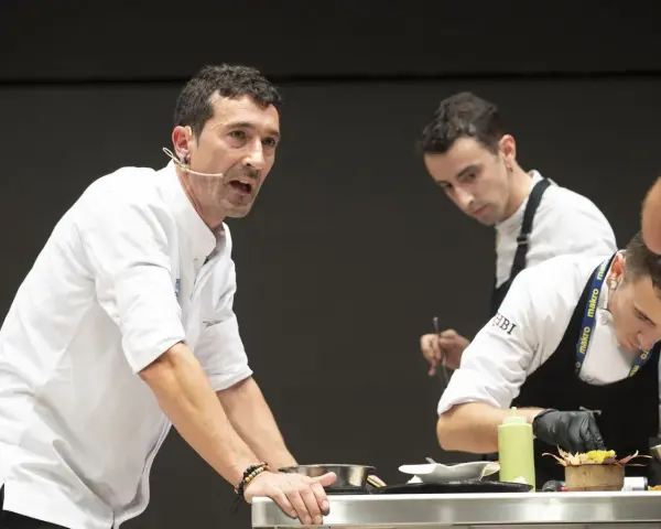 Eneko, chef con micrófono, dirige a su equipo en una demostración culinaria.