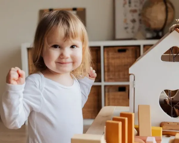 Niña sonriente jugando con bloques, un ejemplo de la evolución del lenguaje en bebés.