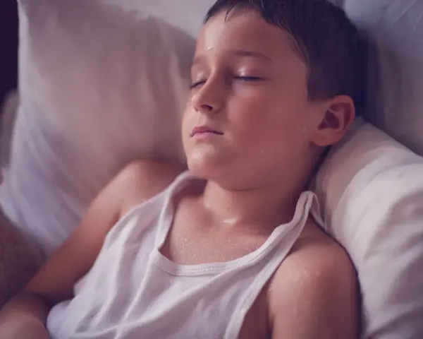 Un niño duerme con la cabeza sudada, quizás por una fiebre o porque un niño suda mucho la cabeza al dormir.