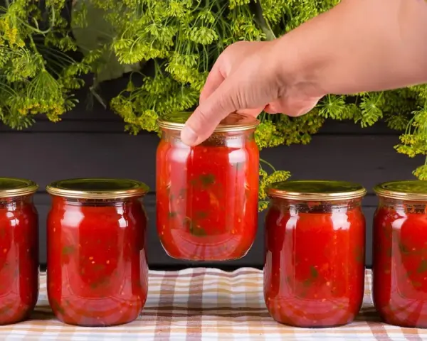Mano toma un bote de cristal con tomate. Prepara para esterilizar botes cristal microondas.