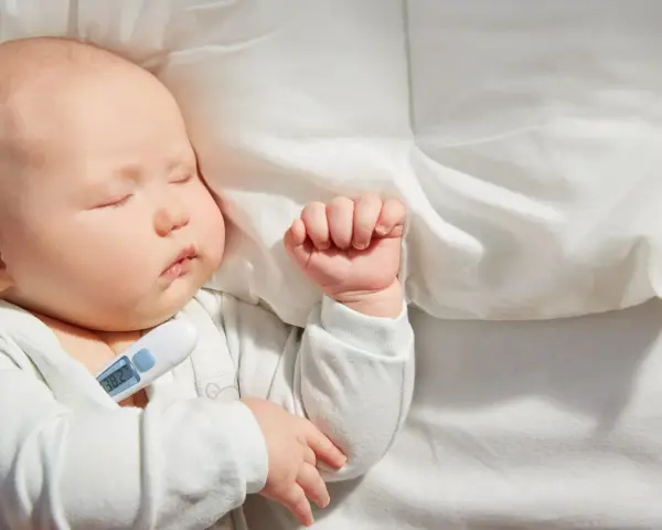 Bebé de 1 mes durmiendo con termómetro que marca 38.2°C, indicando un posible resfriado.