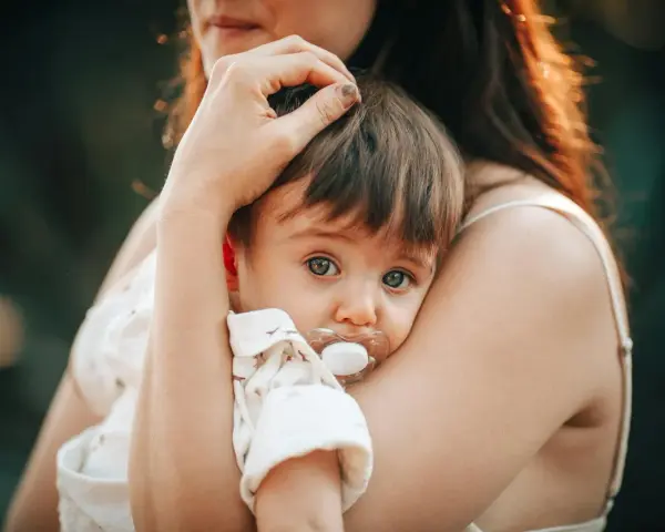 Bebé con chupete, acurrucado en brazos de su madre. Un momento tierno que nos hace pensar en cuando se inventó el chupete.