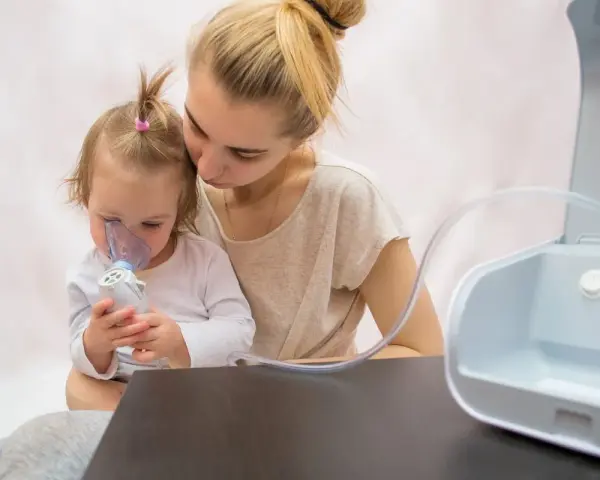 Madre consuela a su hija con bronquitis espástica mientras usa un nebulizador.