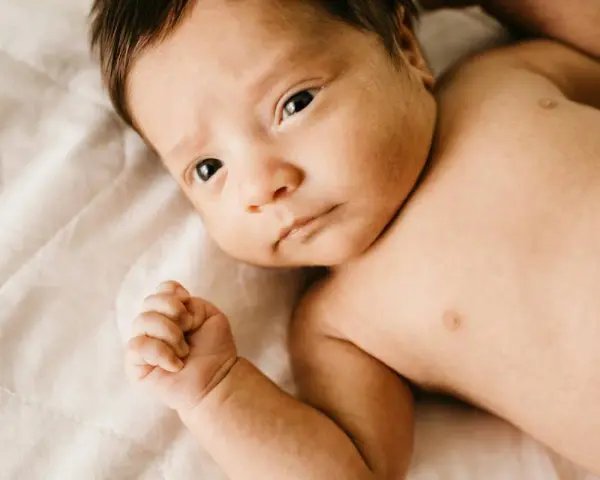 Bebé con mirada intensa, su puño cerrado y piel suave. Podría ser un signo de hipertonía en bebés, pero su expresión es serena.