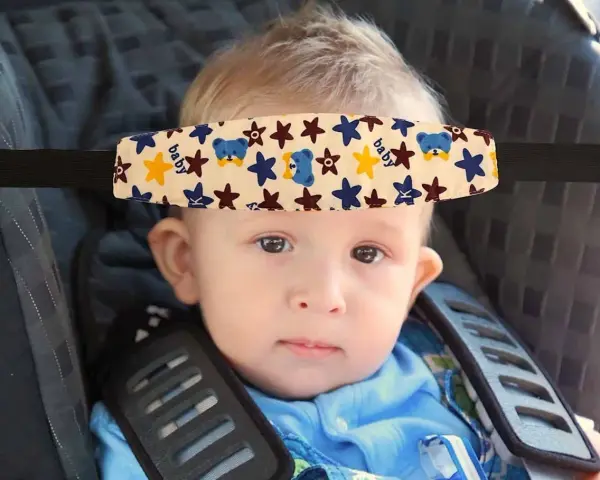Un bebé con un arnés sujetacabezas con ositos y estrellas, esencial porque hay que sujetar la cabeza a los bebés en el coche.