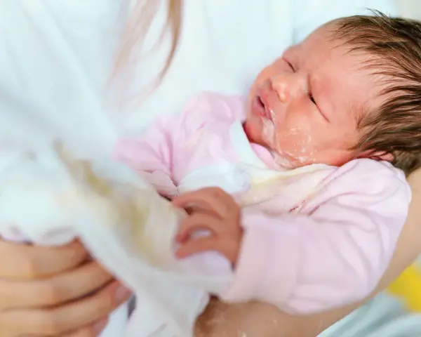 Bebé con leche regurgitada en la cara y ropa. El reflujo en bebés es normal, pero hay que saber cuándo preocuparse.