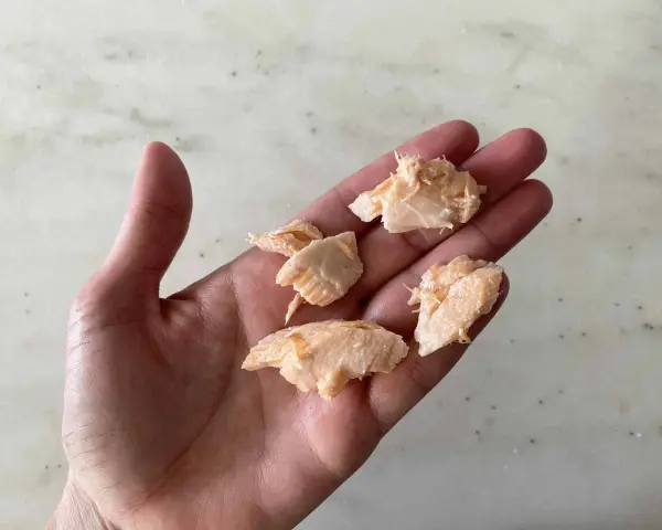 Trozo de salmón desmenuzado en una mano, ideal para saber cuándo dar salmón a un bebé.