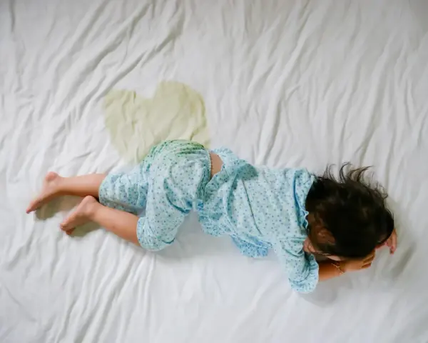Niño en cama con mancha de orina. Buscando enuresis nocturna infantil remedios naturales para ayudarle.