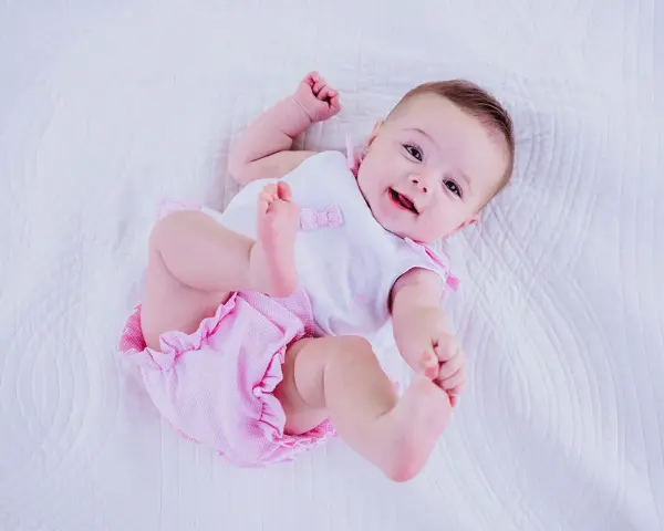 Bebé sonriente con un traje rosa y blanco, perfecto para inspirar nombres de niñas.