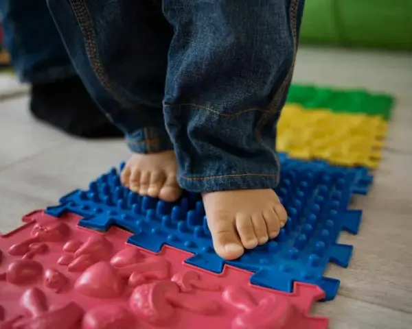 Pies descalzos de un niño sobre un tapete de rompecabezas texturizado, parte de juegos de coordinación para el desarrollo.
