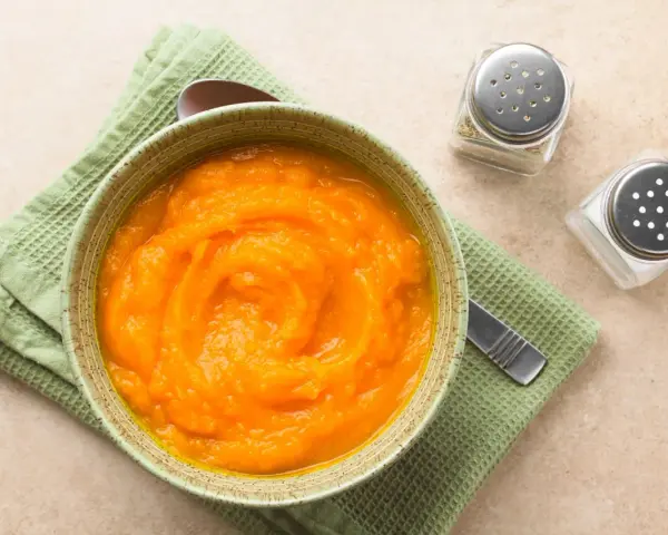 Puré de calabaza y patata para bebé, listo para congelar. Servido en un cuenco con una cuchara y saleros al lado.