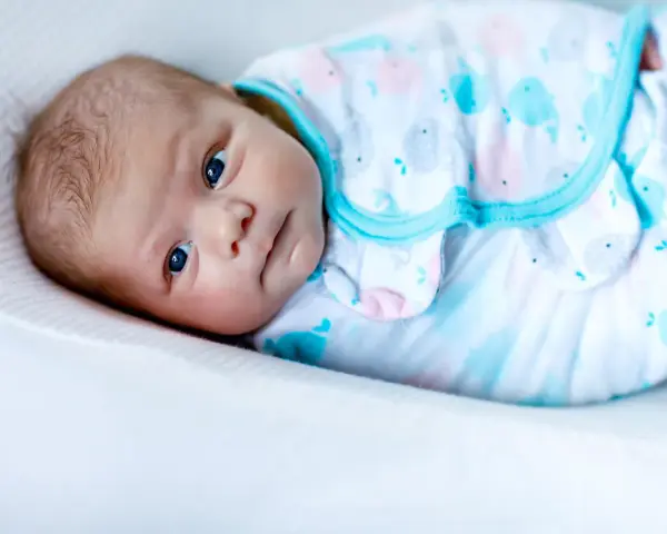 Un tierno bebé con ojos azules, envuelto en una mantita con ballenas, listo para arrullar.