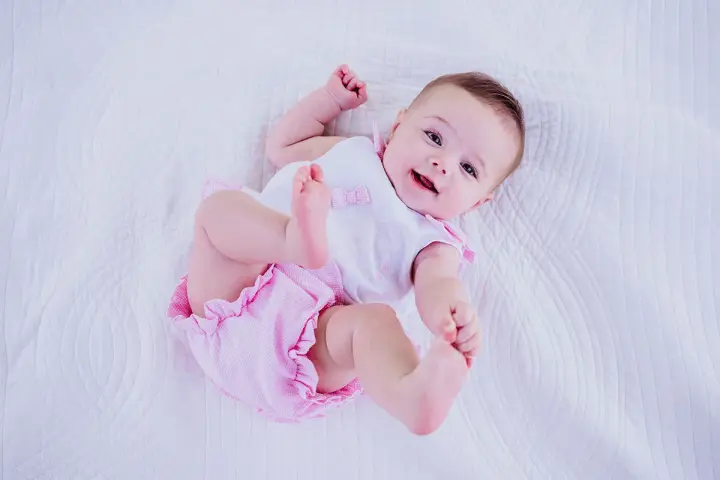 Bebé sonriente con un traje rosa y blanco, perfecto para inspirar nombres de niñas.