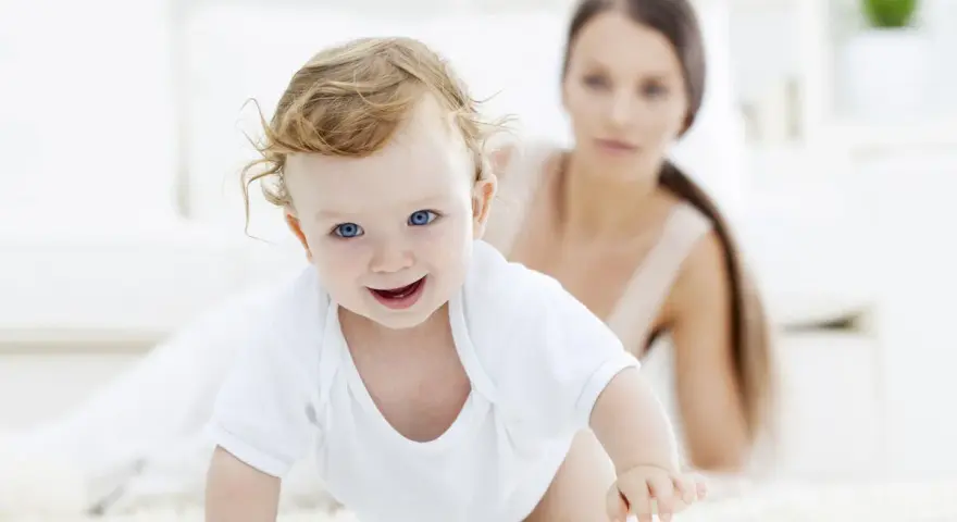 Bebé sonriente gateando, con su madre observando. Una escena tierna para estimular el gateo.
