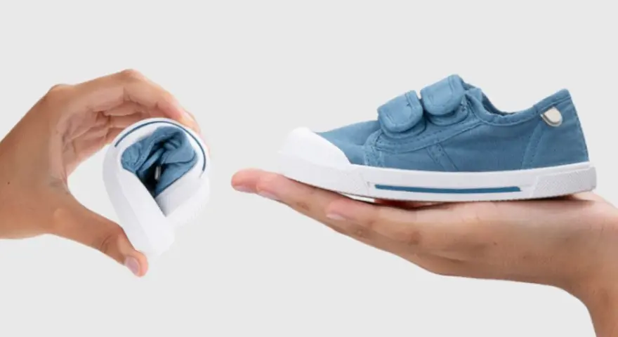Manos muestran que son los escarpines: uno doblado y otro desplegado, de tela azul con velcro.