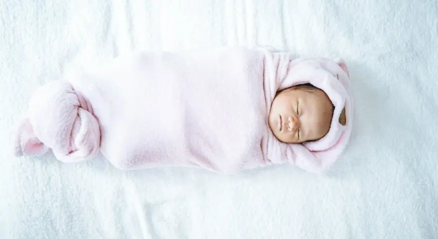 Bebé recién nacido envuelto en manta rosa, durmiendo plácidamente. La temperatura de la casa es ideal para el bebé.