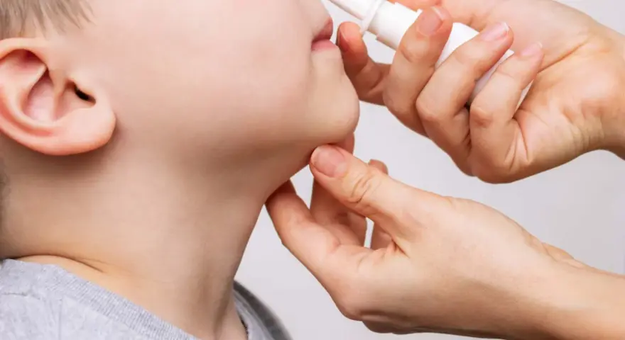 Una mano aplica spray nasal a un niño. La imagen ilustra cuántos lavados nasales se pueden hacer a un bebé para aliviar la congestión.