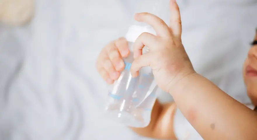Manitas de bebé sujetando un biberón. Se aprecian rojeces en su piel, quizás por dermatitis o por el calor del sudor.