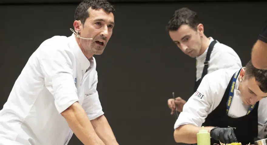 Eneko, chef con micrófono, dirige a su equipo en una demostración culinaria.
