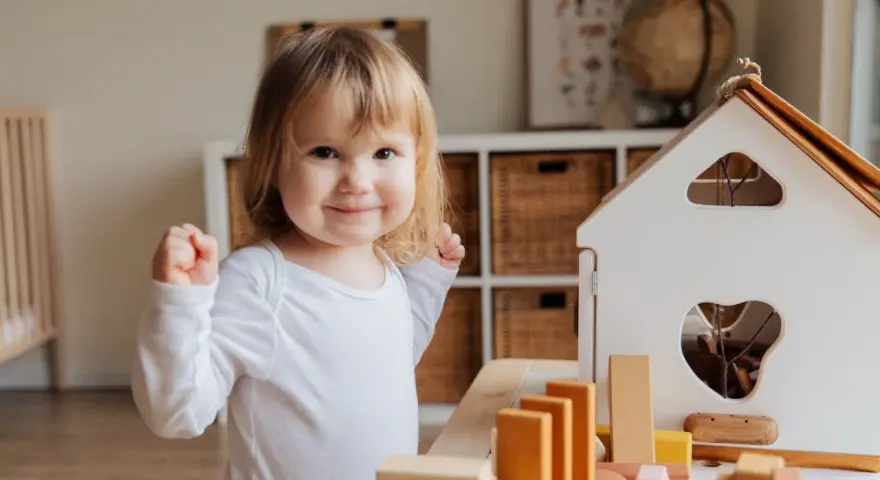 Niña sonriente jugando con bloques, un ejemplo de la evolución del lenguaje en bebés.
