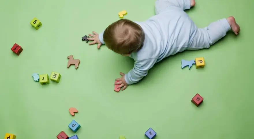 Bebé gateando entre bloques con letras y números, jugando con figuras de animales. Quizás buscando inspiración para nombres de niños originales.