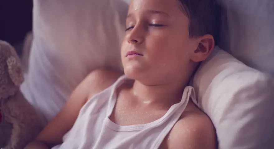 Un niño duerme con la cabeza sudada, quizás por una fiebre o porque un niño suda mucho la cabeza al dormir.