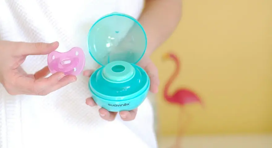 Manos sostienen un chupete rosa y un estuche esterilizador azul. Aprende como esterilizar chupetes fácilmente.