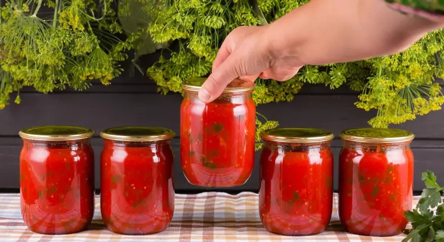 Mano toma un bote de cristal con tomate. Prepara para esterilizar botes cristal microondas.